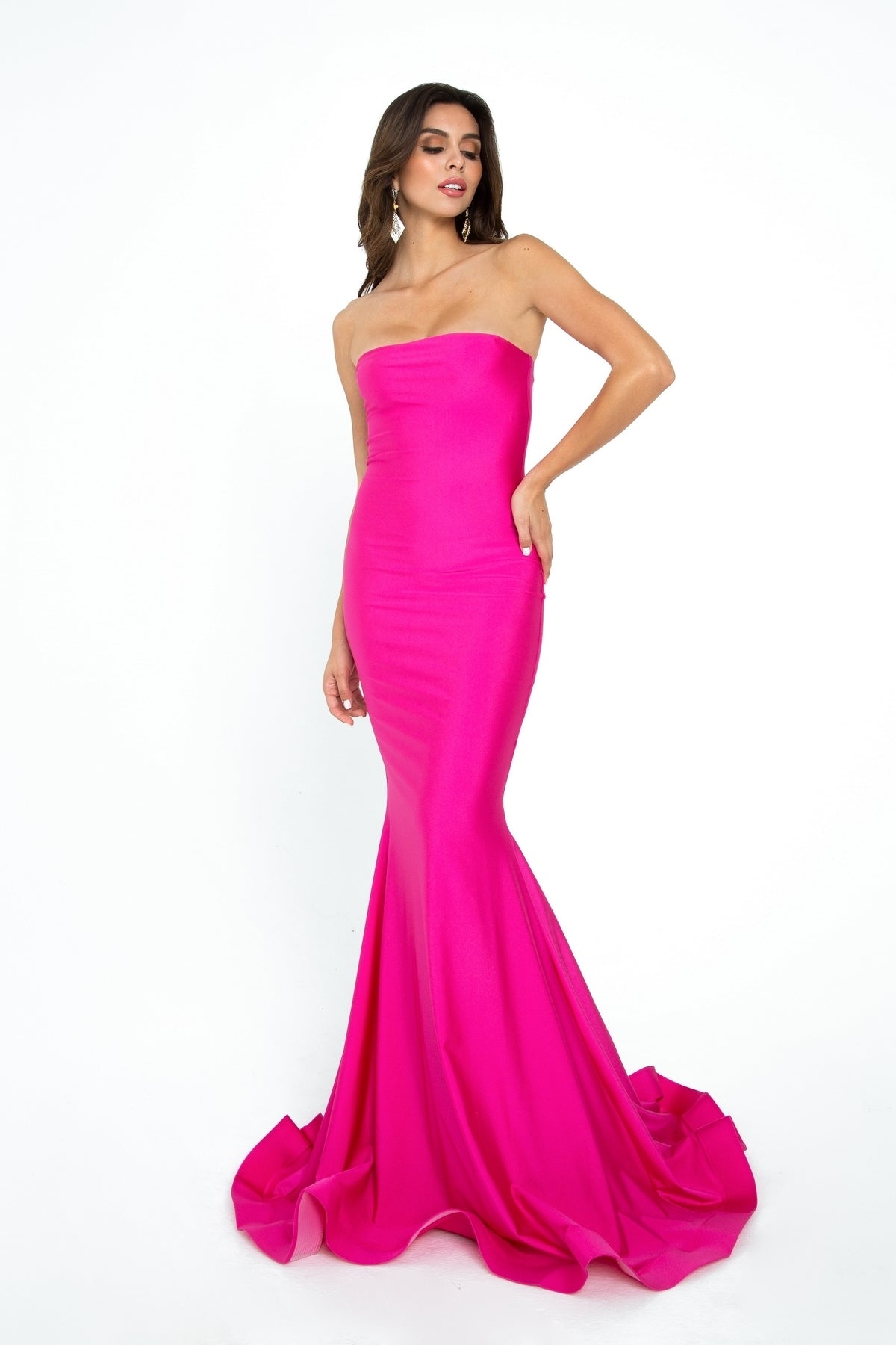 A woman models the Strapless Sleek Long Prom Dress: Atria 6028H, showcasing its fitted bodice and dramatic floor-length hot pink mermaid skirt against a plain white background.